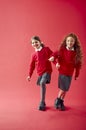 Two Elementary School Pupils Wearing Uniform Linking Arms Against Red Studio Background