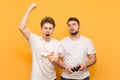 Two emotional friend with joysticks in their hands play video games, isolated on a yellow background. Winner and loser are playing Royalty Free Stock Photo