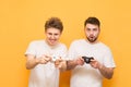 Two emotional gamer with gamepad in hand, playing video games focused on a yellow background looking into the camera. Two friends