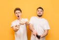 Two emotional men, a teenager and a man with a beard, are on a yellow background with joysticks in their hands and expressively Royalty Free Stock Photo