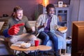 Two emotional sports fans watching TV and eating snacks