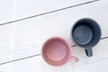 Two empty ceramic mugs, pink and blue-grey, isolated on white painted wood from above. Space for text