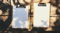 Two empty clipboards with blank sheets on a wooden table, dappled by sunlight and soft shadows from overhead leaves. Royalty Free Stock Photo