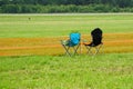 Two empty folding chairs at orange plastic barrier mesh at the edge of a green field