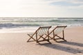 Two empty folding wooden chairs on shore at beach in front of waves splashing in sea against sky