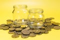 Two empty glass jars on the background of a scattering of coins yellow background. Royalty Free Stock Photo