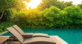 Two empty lounge chairs positioned on a wooden deck beside a tranquil swimming pool surrounded by lush greenery Royalty Free Stock Photo