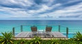 Two empty lounge chairs on a wooden deck overlooking a turquoise ocean and cloudy sky Royalty Free Stock Photo