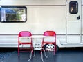 Two empty red iron chairs with white round table in front of the door and window of caravan car with nobody. Royalty Free Stock Photo