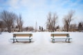 two empty snow-covered benches with footprints leading away Royalty Free Stock Photo