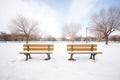 two empty snow-covered benches with footprints leading away Royalty Free Stock Photo