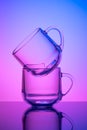 Two empty tea cups on a pink and blue neon background. Drinking glass. Dark silhouette, night illuminated effect. Glassware.