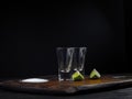 Two empty tequila shot with lime and sea salt on a wooden board and dark background