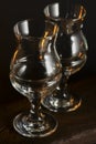 Two empty tulip beer glasses on dark wooden table over black background.