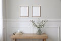 Two empty vertical picture frame mockups hanging on wall. Cup of coffee, books. Wooden desk, table. Vase, green grasses