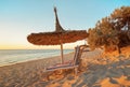 Two empty wooden sunbeds facing the sunset, sea in background, straw sun shade above, image illustrating tropical Royalty Free Stock Photo