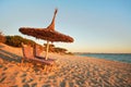 Two empty wooden sunbeds facing the sunset, sea in background, straw sun shade above, image illustrating tropical vacation Royalty Free Stock Photo