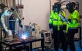 Two engineer or technician worker men with face mask protection of light stand in front of welding robotic arm machine is working Royalty Free Stock Photo