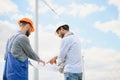 Two engineers discussing against turbines on wind turbine farm. Royalty Free Stock Photo