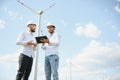 Two engineers discussing against turbines on wind turbine farm. Royalty Free Stock Photo