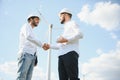 Two engineers discussing against turbines on wind turbine farm. Royalty Free Stock Photo