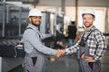 Two engineers in hard hats shake hands in a factory. Royalty Free Stock Photo