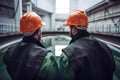 Two engineers in hardhats discussing something while standing in a factory, Two industrial engineers are in the rearview wearing