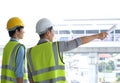 Two engineers man standing in front of the site. Right engineer holding paper roll and point to construction area Royalty Free Stock Photo