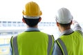 Two engineers man standing in front of the site. Right engineer holding paper roll and point to construction area Royalty Free Stock Photo