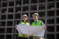 two engineers, a man and a woman in white helmets and protective vests, work at the construction site.