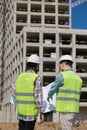 two engineers, a man and a woman in white helmets and protective vests, work at the construction site.