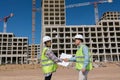 two engineers, a man and a woman in white helmets and protective vests, work at the construction site.