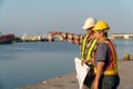 Two engineers stood wearing a safety helmet. Standing at the pier And holding the blueprint And consult the plan In the constructi