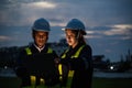 Two engineers, wearing helmets and reflective vests, work on a laptop at night at an industrial site. Industrial plant and Royalty Free Stock Photo