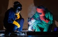 Two engineers working in the dark at nighttime. Mechanics wearing a mechanic coveralls work together to weld the metal rod, making