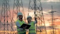 Two engineers are working in front of ETL constructions. Industrial workers near power line.