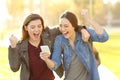 Excited friends watching phone content in a park Royalty Free Stock Photo