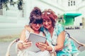 Two excited senior women using tablet and watching media content on line with a laptop  in cafe Royalty Free Stock Photo