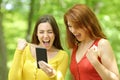Two excited women checking smart phone in a park Royalty Free Stock Photo