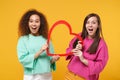 Two excited women friends european and african american girls in pink green clothes posing isolated on yellow wall Royalty Free Stock Photo