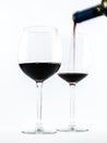 Two exquisite transparent glasses with red wine and a bottle pouring wine on a white background Royalty Free Stock Photo