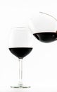 Two exquisite transparent glasses with red wine - one pouring wine into the other - on a white background Royalty Free Stock Photo
