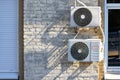 Two external air conditioners installed outside on an old brick wall near new metal-plastic windows