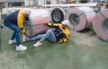 Two factory worker are carefully handling a large roll of steel, but one worker appear to have injured his leg