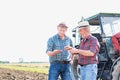 Two farmers examining soil while standing against tractor in field