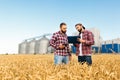 Two farmers stand in a wheat field with tablet. Agronomists discuss harvest and crops among ears of wheat with grain Royalty Free Stock Photo