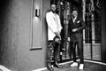 Two fashion black men pose against house with garlands. Fashionable portrait of african american male models. Wear suit, coat and Royalty Free Stock Photo