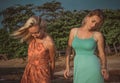 Two fashion models posing in red and turquoise dresses in the rays of the setting sun on a tropical beach Royalty Free Stock Photo