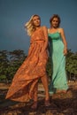 Two fashion models posing in red and turquoise dresses in the rays of the setting sun on a tropical beach Royalty Free Stock Photo