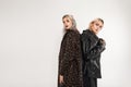 Two fashionable girlfriends in oversized fashionable youth clothes stand with their backs to each other in studio. Sexy girl in